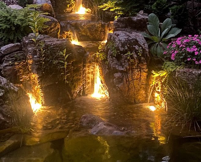 Illuminated rock garden with cascading waterfalls at night.